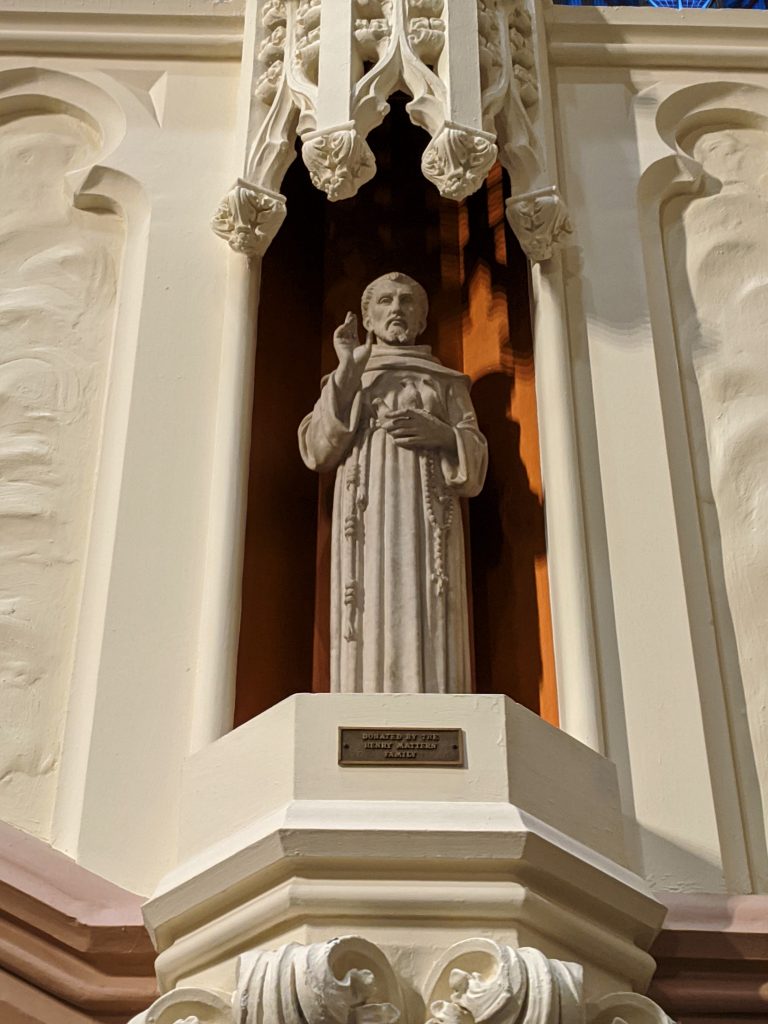 A small light grey stone statue of Saint Francis of Assisi