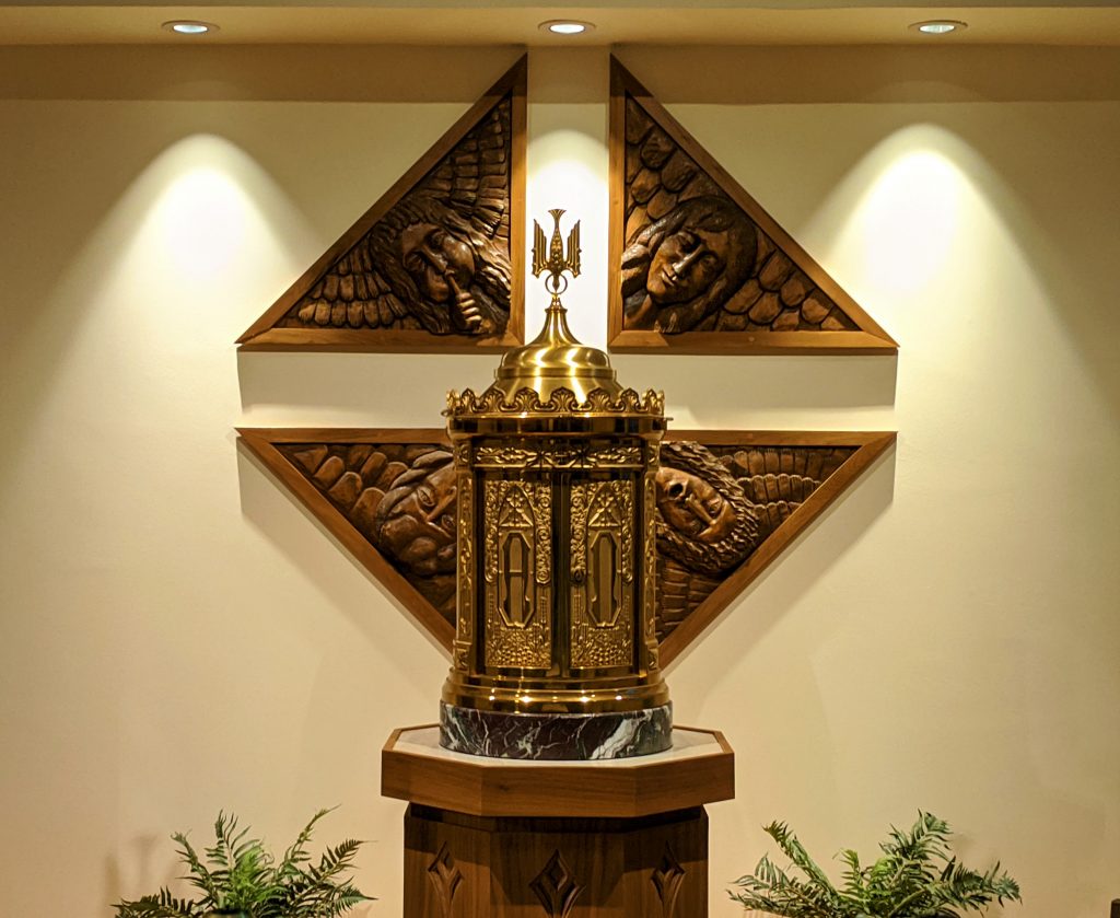 The tabernacle in the chapel/ Behind the gold colored tabernacle are wooden carvings of the Four Evangelists Matthew, Mark, Luke, and John.