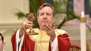 Bishop McClory elevates the chalice and plate at Mass. He is dressed in red vestments with a gold accent.